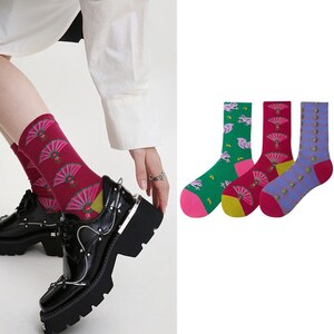 Könnte beinhalten: Drei Paar bunte Socken mit verschiedenen Mustern. Ein Paar hat ein rosa, grünes und gelbes Fächermuster, ein anderes Paar hat ein rosa, grünes und gelbes Einhornmuster und das letzte Paar hat ein lila, blaues und grünes geometrisches Muster.