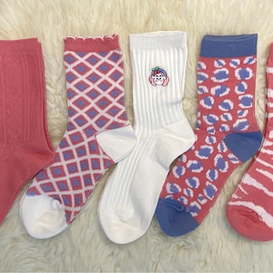 Könnte beinhalten: Fünf Paar Socken mit verschiedenen Mustern. Die Socken sind rosa, weiß und blau mit geometrischen, tierischen und gestickten Designs.