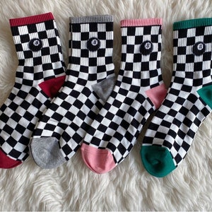 Op de afbeelding: Vier paar zwart-wit geblokte sokken met verschillende gekleurde hakken en tenen. De sokken hebben een kleine zwarte cirkel met een wit nummer 8 in het midden.