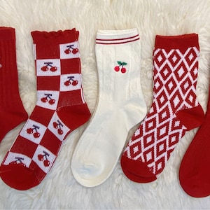 Könnte beinhalten: Fünf Paar rote Socken mit verschiedenen Mustern. Ein Paar hat ein kariertes Muster mit Kirschen, ein Paar hat ein Rautenmuster, ein Paar hat ein Kirschendesign, ein Paar hat eine gerippte Struktur und ein Paar hat ein kleines gesticktes Design.