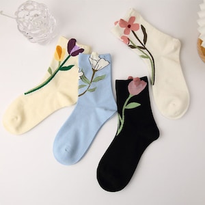 Puede incluir: Cuatro pares de calcetines de tobillo con diseños florales. Los calcetines son de color blanco, azul claro, negro y crema. Cada calcetín tiene un diseño floral diferente.