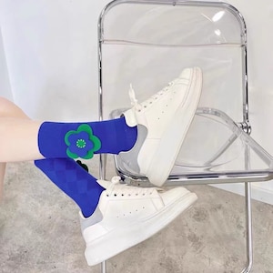 Könnte beinhalten: Ein Paar blaue Socken mit einem grünen und blauen Blumendesign auf einer Socke. Die Socken werden mit weißen Turnschuhen getragen.