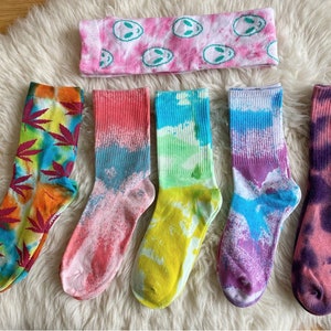 Può includere: Sei paia di calzini tie-dye colorati con diversi motivi. I calzini sono disposti su una superficie bianca e soffice.