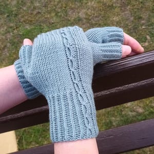 May include: A pair of light blue fingerless gloves, knitted with a cable design on the upper hand. The gloves are made of a soft, textured yarn and are designed to keep hands warm while leaving fingers free.