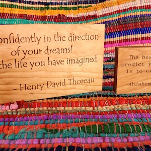 May include: Two wooden signs with inspirational quotes. The first sign reads "Go confidently in the direction of your dreams! Live the life you have imagined. - Henry David Thoreau". The second sign reads "The best way to predict your future is to create it. - Abraham Lincoln".