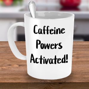 May include: White ceramic coffee mug with black text that reads "Caffeine Powers Activated!"