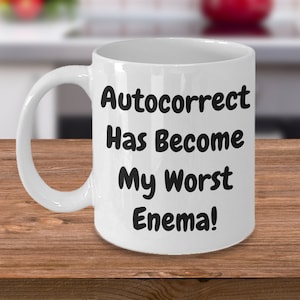 May include: White ceramic coffee mug with black text that reads "Autocorrect Has Become My Worst Enema!"