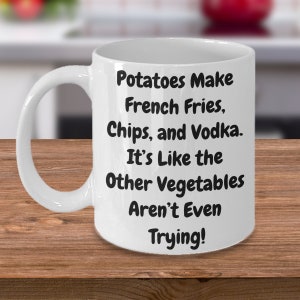 May include: White ceramic coffee mug with black text that reads "Potatoes Make French Fries, Chips, and Vodka. It's Like the Other Vegetables Aren't Even Trying!"