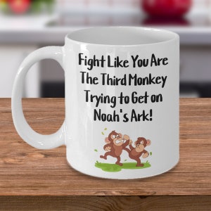 May include: White ceramic coffee mug with a black graphic that reads "Fight Like You Are The Third Monkey Trying to Get on Noah's Ark!" Two cartoon monkeys are fighting on a green patch of grass.