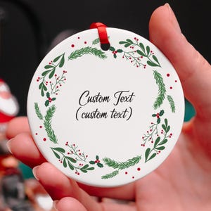 May include: White round ceramic ornament with a green and red holly wreath border. The ornament has the text "Custom Text (custom text)" in the center.