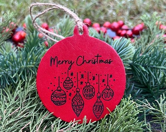 May include: Red Christmas ornament with the text "Merry Christmas" and a design of six black and white ornaments hanging from a string.