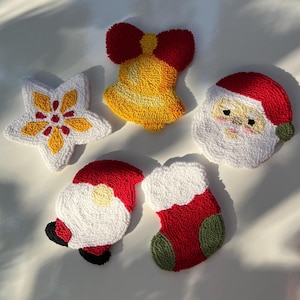 May include: Five Christmas-themed felt ornaments: a red and yellow bell with a red bow, a white star with a yellow centre, a red stocking with a green cuff, and two Santa Claus faces with red hats and white beards.