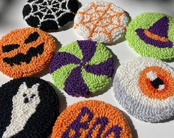 May include: Eight handmade Halloween-themed felt ornaments. The ornaments are round and feature various designs, including a pumpkin, a ghost, a witch's hat, a spiderweb, and the word "BOO".