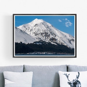 May include: A framed photograph of a snow-capped mountain peak against a blue sky. The mountain is surrounded by trees and water. The frame is black and the image is 24x36 inches.