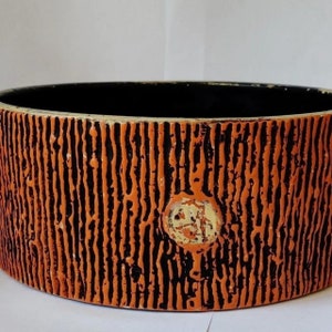 May include: Orange and black ceramic planter with a textured surface and a circular design in the centre.
