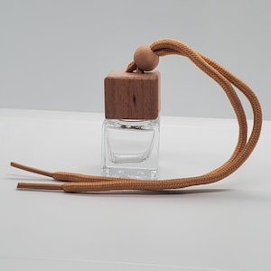 May include: A clear, square glass bottle with a wooden cap and a tan cord for hanging. The wooden cap is a cube shape with a small wooden bead. The cord is looped and has two finished ends.