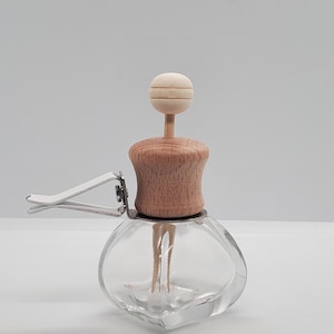 May include: A clear glass car air freshener with a wooden top and a wooden ball on top. The air freshener has a metal clip for attaching to a car vent. The wooden parts are light brown.