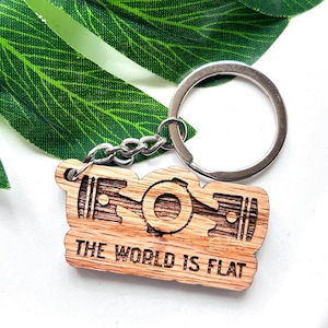 Puede incluir: Llavero de madera con un diseño de pistón y el texto "The World Is Flat".