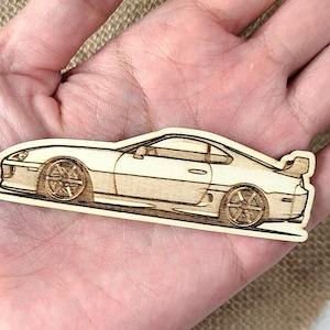 May include: A wooden cutout of a white Toyota Supra sports car. The car is in profile view and has black wheels.