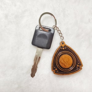 Könnte beinhalten: Ein Holzschlüsselanhänger mit einem schwarzen und braunen Rotationsmotordesign. Der Schlüsselanhänger ist an einem silbernen Schlüsselring und einem schwarzen Autoschlüssel befestigt.