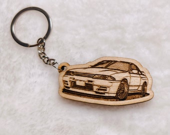 May include: A wooden keychain featuring a detailed laser-engraved illustration of a white sports car. The keychain is attached to a silver metal ring.