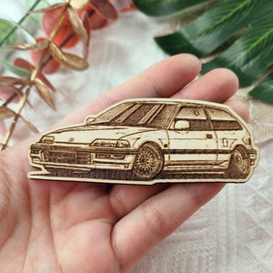 May include: A wooden cutout of a white Honda Civic, a popular car model, with detailed lines and a realistic design.