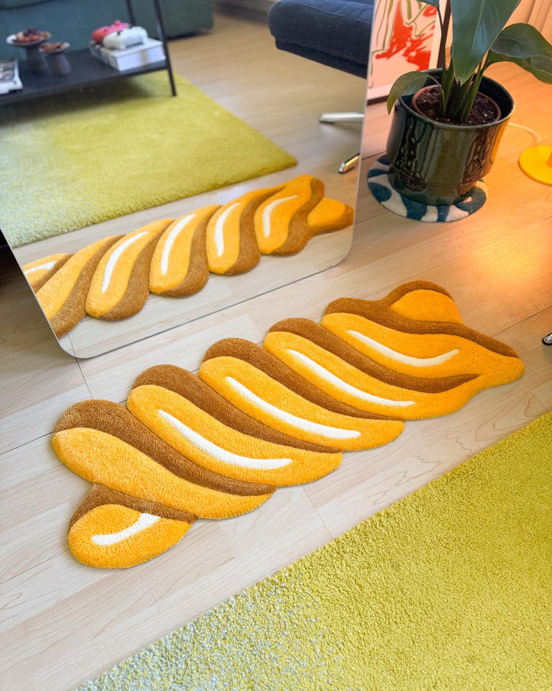 K&ouml;nnte beinhalten: Ein abstrakter Teppich in Gelb-, Braun- und Wei&szlig;t&ouml;nen. Der Teppich hat eine wellenf&ouml;rmige, l&auml;ngliche Form mit einer strukturierten Oberfl&auml;che. Das Design zeigt abwechselnde Streifen in Gelb, Braun und Wei&szlig;, wodurch ein ansprechendes Muster entsteht.