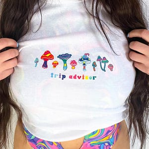 May include: White cropped t-shirt with a colorful mushroom graphic and the text "trip advisor".