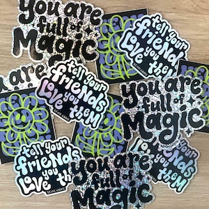 Peut inclure: Plusieurs autocollants avec du texte holographique et noir. Les autocollants présentent des phrases telles que "You are full of Magic" et "Tell your friends you love them." Certains autocollants ont un motif floral avec un smiley.