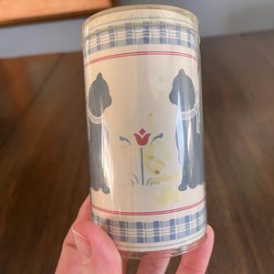 May include: A roll of vintage wallpaper featuring a repeating pattern of blue cat silhouettes, red stripes, and a blue and white plaid design. The wallpaper has a cream-colored background and a floral accent.