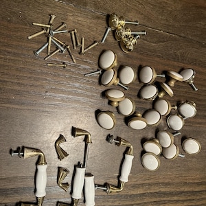 May include: A collection of cabinet hardware including round white ceramic knobs with brass-toned bases, arched drawer pulls with white ceramic centers and brass-toned metal ends, and a set of assorted metal mounting screws and bolts.