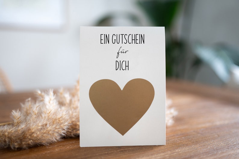 May include: A white card with the text "EIN GUTSCHEIN f&uuml;r DICH" and a gold heart in the center.