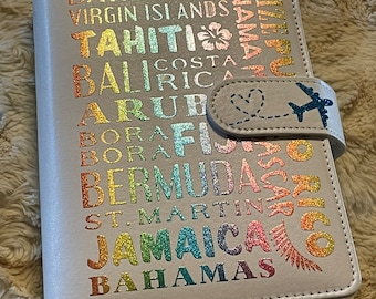 May include: A white travel journal with a rainbow glitter design featuring the names of various islands and destinations, including Hawaii, Barbados, Virgin Islands, Tahiti, Bali, Aruba, Bora Bora, Bermuda, St. Martin, Jamaica, and Bahamas.