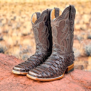 May include: A pair of brown leather cowboy boots with intricate stitching and a scaly pattern. The boots have a pointed toe and a low heel.