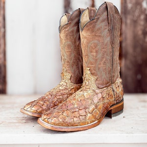 May include: A pair of brown leather cowboy boots with gold accents and a patterned design. The boots are made of a textured material that resembles alligator skin.