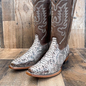 May include: A pair of brown leather cowboy boots with a snakeskin pattern. The boots have a pointed toe and a decorative stitch pattern on the shaft.