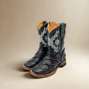 May include: A pair of black leather cowboy boots with intricate white stitching and a unique textured design on the vamp. The boots have a brown sole and a tan interior lining. The Agave Boots logo is visible on the pull tab.