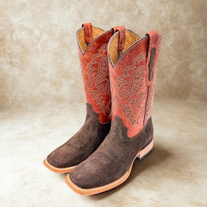 May include: A pair of square-toe cowboy boots featuring dark brown suede vamps and shafts with distressed red leather uppers. The red leather sections are decorated with intricate tonal stitching patterns and include pull tabs at the top edges.