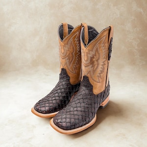 May include: A pair of cowboy boots with a brown and black textured design. The boots have a square toe and a tan leather upper with decorative stitching. The lower part of the boot is a dark brown, textured material.