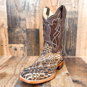 Puede incluir: Una bota de vaquero de cuero marr&oacute;n con un dise&ntilde;o tejido en el pie y un patr&oacute;n cosido decorativo en la ca&ntilde;a. La bota tiene una puntera cuadrada y un tac&oacute;n apilado. La paleta de colores incluye tonos de marr&oacute;n, beige y crema.