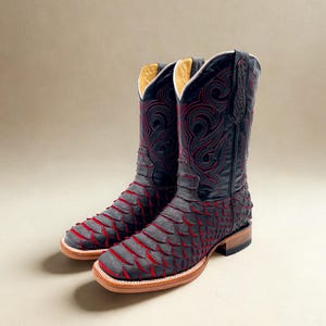 May include: A pair of black cowboy boots with red stitching and accents. The boots feature a unique scale-like pattern on the foot and intricate embroidery on the shaft. The soles are a light brown color.