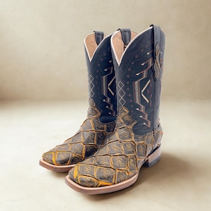 May include: A pair of cowboy boots with a square toe. The boots have a black shaft with geometric embroidery and a brown and yellow patterned vamp. The soles are light brown.