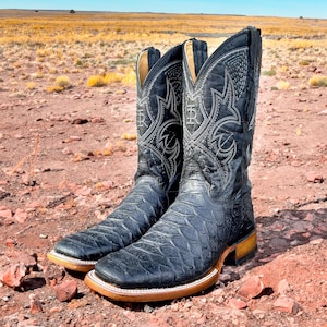 May include: A pair of black cowboy boots with intricate stitching and a textured leather design. The boots have a pointed toe and a low heel.