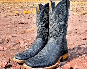 May include: A pair of black cowboy boots with intricate stitching and a textured leather design. The boots have a pointed toe and a low heel.