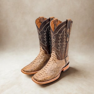 May include: A pair of cowboy boots with a snakeskin pattern on the foot and a brown leather upper. The boots have a square toe and decorative stitching. The background is a neutral beige.