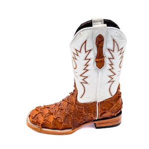 May include: A cowboy boot with a white shaft featuring brown decorative stitching. The vamp is made of textured brown leather. The boot has a square toe and a stacked heel.