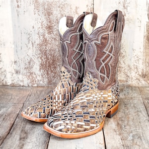 May include: A pair of brown leather cowboy boots. The boots feature a woven pattern on the foot and a decorative stitched design on the upper shaft. The boots have a square toe and a stacked heel.