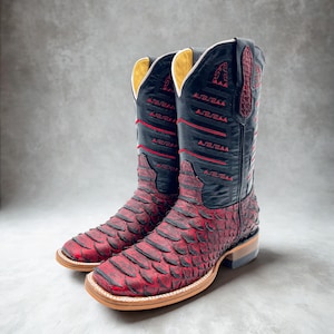 May include: A pair of cowboy boots with a red and black design. The boots have a textured, scaly pattern on the lower part and a smooth black upper with red accents. The soles are light brown.