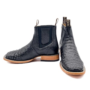 May include: A pair of black leather ankle boots with a square toe and a textured, crocodile-like pattern. The boots have a pull tab at the back and a light brown sole. The brand name "IRON RANCH" is visible on the back of one boot.