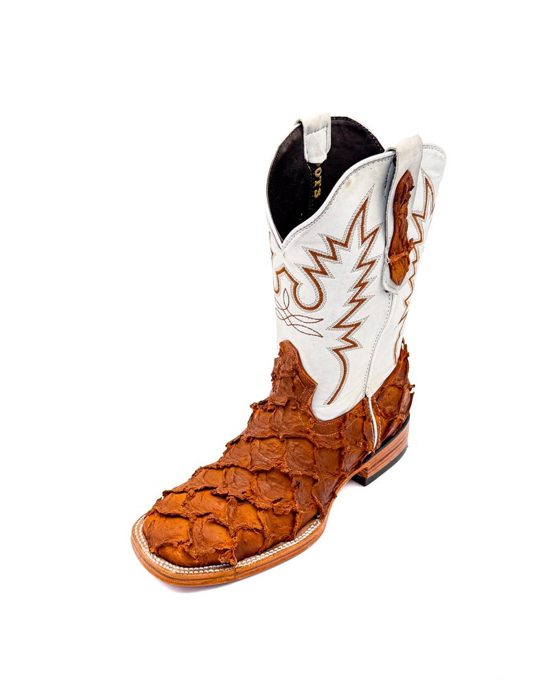 May include: A single cowboy boot with a square toe. The boot features a white shaft with brown stitching and a brown, textured vamp. The boot is made of leather and has a stacked heel.